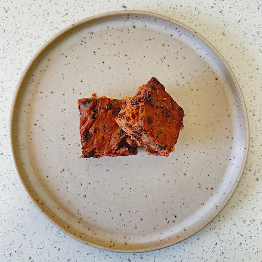 Sweetpotato Brownie - Cut Bulk RestTwo pieces of brown food on a speckled ceramic plate on a light surface.