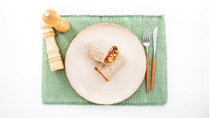 Two pieces of bread with a topping on a white plate with a green placemat, accompanied by a pepper grinder, fork, and knife.