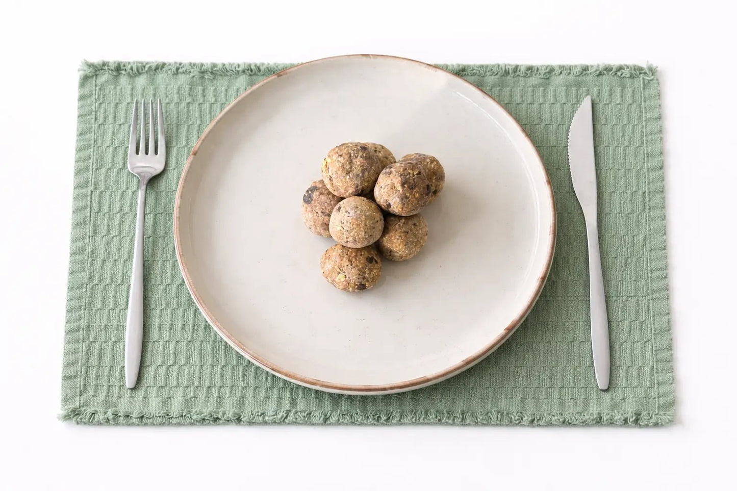 Coconut, Peanut, Chocolate Energy Ball - Cut Bulk RestWhite plate with brown food on a green placemat with silver fork and knife