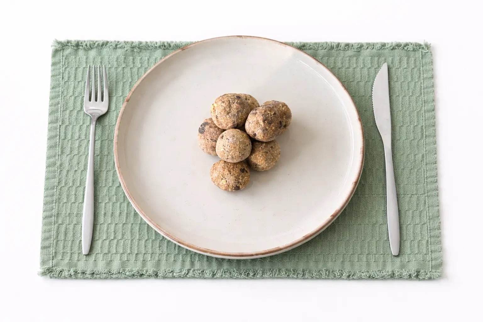 Coconut, Peanut, Chocolate Energy Ball - Cut Bulk RestWhite plate with brown food on a green placemat with silver fork and knife