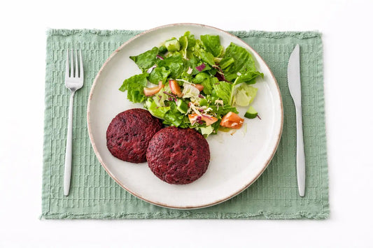 Quinoa Beetroot Burger/Salad - Cut Bulk RestTwo beet burgers on a plate with a side salad on a green placemat.